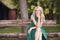 One young woman portrait, sitting in wood bench, green dress, 25 years old, smiling happy, looking to camera.