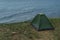 Onely green small tent stands on grass shore of blue Lake Baikal, sea waves and ripples, summer