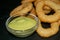 Onion rings and a glass saucepan with sauce. Close up