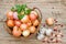 Onions in a wicker basket and garlic on a wooden table