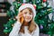 Online Christmas greetings. A close-up portrait of a cute girl in a New Year`s hat with a mobile phone. The child uses gadgets to