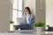 Online communication. Young woman sitting on windowsill at home and talking to family, friend or coworker on laptop