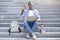 Online education. African American student with laptop, backpack and books showing okay gesture on stairs outdoors