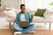 Online shopping at home. Cheerful young black guy in jeans with laptop shows credit card, sits on floor