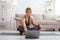 Online stream workout. Woman sitting in lotus pose with laptop in living room interior