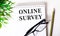 ONLINE SURVEY is written in a white notebook next to a pencil, black-framed glasses and a green plant