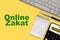 ONLINE ZAKAT Islamic tax  text with notepad, calculator, keyboard and fountain pen on yellow background