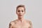 Oops. Portrait of half naked tattooed woman with short hair feeling awkward, silly isolated over light background