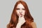 Oops... Portrait of young and beautiful redhead woman touching her lips and looking at camera while standing against