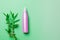 Opaque cosmetic bottle lying near bamboo on green background with copy space