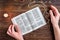 Open bible, candle, christian cross and human hands on wooden background. Prayer to God