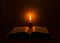 Open Bible illuminated by a single candle