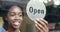 Open, black woman and business owner with a door sign to welcome customers or clients in retail store. Employees