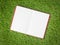 Open blank book on artificial green grass