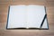 Open blank paper leather notebook with pen on wooden table.