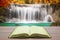 open book with beautiful autumn waterfall in deep forest background