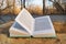 An open book in blue bound lying on a stump background of the nature forest trees road. Turn pages