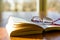 Open book and glasses on a wooden table with sunlight