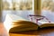 Open book and glasses on a wooden table with sunlight