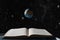 An open book, a levitating model of the planet earth levitates above it, against the background of outer space with stars. The