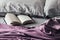 Open book on the messy bed with a purple bedspread and gray pillows. Fascinating book in soft crumpled bedding