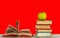 Open book textbook, pile of books and green apple on a wooden desk on the red background. Back to school distance home education.