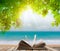 Open book on wood floor with green grass and leaf over beach sea