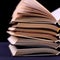 Open books are stacked on the desk, on a black background, isolate. Difficult homework at school, a mountain of knowledge