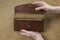 Open brown stitched wallet in female hands on a gray background