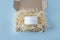 Open cardboard box package with shredded paper and cream jar on blue background. Gift craft paper box. Eco friendly pack. Natural