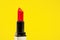 Open completely twisted lipstick in bright red color for passionate makeup for party or date, yellow background, front