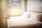 Open Door to bed in hotel room bedroom white bed sheets lit by natural warm nature sunlight from window at morning time