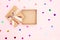 Open gift box with kraft cardboard bow on pink background with confetti, top view. Surprise concept, birthday present