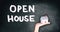 Open house real estate sale sign on black chalkboard texture with realtor hand showing home. House hunting