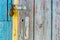 Open iron padlock on a battered wooden door with weathered cracks of blue and yellow colors of old country house
