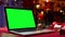 Open laptop with green screen chroma key stands on a red table next to gifts and toys. Home room with Christmas decor
