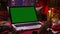 Open laptop with green screen chrome key on table among Christmas gift boxes and decorations with garland lights on