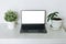 Open laptop with white screen on table with green house plants, mockup