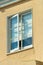 Open lone window with white trim and curtains on a beige stucco house in midday sun in the neighborhood or in the city
