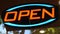 Open neon sign glowing in the dark. Vivid retro styled text at entrance on glass window. Colorful electric banner selective focus