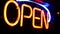 Open neon sign glowing in the dark. Vivid retro styled text at entrance on glass window. Colorful electric banner selective focus