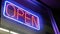 Open neon sign glowing in the dark. Vivid retro styled text at entrance on glass window. Colorful electric banner selective focus