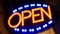 Open neon sign glowing in the dark. Vivid retro styled text at entrance on glass window. Colorful electric banner selective focus