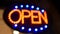 Open neon sign glowing in the dark. Vivid retro styled text at entrance on glass window. Colorful electric banner selective focus