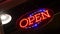 Open neon sign glowing in the dark. Vivid retro styled text at entrance on glass window. Colorful electric banner selective focus