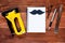 Open notebook with black mustache and tools on a brown wooden background. concept of shopping planning for repairs