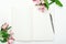 An open notebook with a steel pen on a white wooden background with flowers. Minimal composition, home women`s office