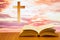 Open old bible on a wood table with blurred cross & colourful clouds and sky as background