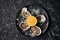 Open oysters lying on a black plate on crushed ice with lemon, with a knife for opening oysters on a dark textured stone