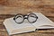 Open paper book and round reading glasses on wooden background with copy space